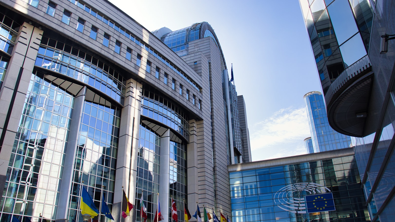 Modern EU parliament building with flags and sky in Brussels — the institutions behind ECSP and MiFID II rules.